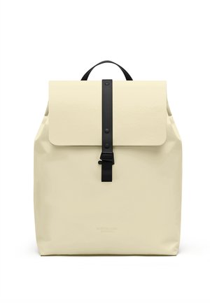 Rygsæk i cremefarve med sort strop og spænde, en topstrop og en rektangulær klap, der dækker hovedrummet.