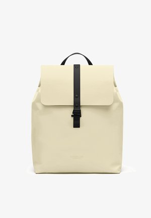 Zaino color crema con tracolla nera e chiusura a fibbia, manico superiore e patta rettangolare che copre il vano principale.