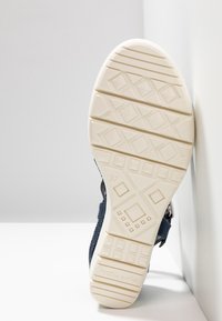 Chaussure bleu marine avec une tige en tissu texturé, dotée d'une semelle extérieure en caoutchouc blanc avec une bande de roulement à motif et la taille 37 marquée sur le côté.