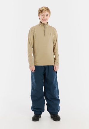 T-shirt à manches longues tan avec demi-zip et logo, associé à un pantalon bleu imperméable, tous deux conçus pour l'activité en extérieur, avec des poignets élastiques.