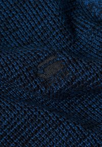 Tessuto a maglia testurizzato in blu scuro e nero, caratterizzato da un motivo sottile. Include un piccolo etichetta nera vicino al bordo.