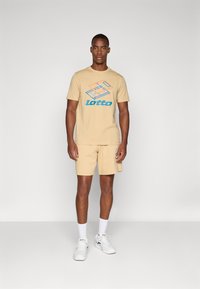 Beige cotton t-shirt with blue and orange graphic text "lotto" and design elements, paired with matching beige shorts and white sneakers.