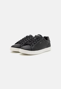 Zapatillas bajas de cuero negro con suelas de goma blanca, que cuentan con un panel trasero texturizado en gris oscuro y seis ojales para los cordones negros.
