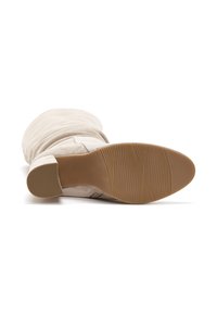 Botte de cheville en daim beige avec un bout rond et un talon carré. La semelle est en caoutchouc avec un motif de grip texturé. Présente un design drapé.