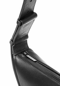 Zbliżenie na teksturowany czarny skórzany pasek torby i suwak z metalowym uchwytem z wygrawerowaną nazwą marki.