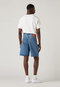 Denimshorts i mellomblå med rett passform, baklommer og en merket skinnlapp. Kombinert med en hvit t-skjorte og hvite joggesko.