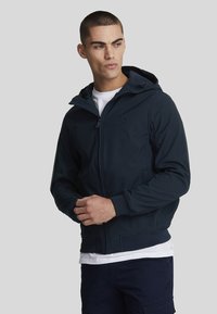 Jacket con cappuccio blu navy realizzata in tessuto morbido, dotata di zip completa, due tasche frontali e un logo sottile sul petto.