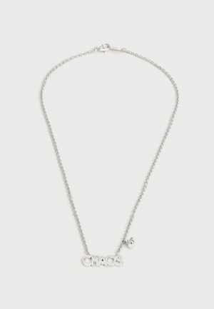 Collier à chaîne argentée avec un fermoir, un pendentif portant le mot « CHAOS » et un petit charm suspendu sur un fond uni.