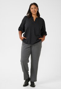 Blouse noire à manches longues avec un motif texturé, décolleté en V, manches bouffantes ; associée à un pantalon large gris et des bottines noires.