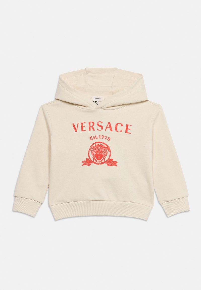 Φούτερ σε κρεμ χρώμα με κόκκινο λογότυπο Versace, κεφάλι Μέδουσας και το κείμενο "Est. 1978" μπροστά, απλωμένο επίπεδα σε λευκό φόντο.