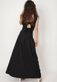 Czarna maxi sukienka z dopasowanym gorsetem i dużym wycięciem na plecach, z kokardą w talii, wykonana z miękkiego materiału i szeroką rozkloszowaną spódnicą.