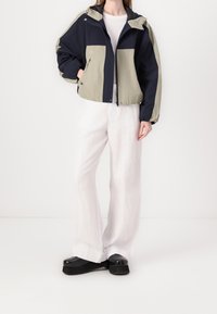 Färgsorterad jacka med marinblå och ljus olivgröna paneler; tillverkad av lättviktigt tyg med huva, dragkedjestängning och framfickor.