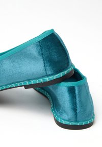 Zapatos de terciopelo en tonos verde azulado, con un ribete y costuras en contraste turquesa, textura suave y suela negra plana.