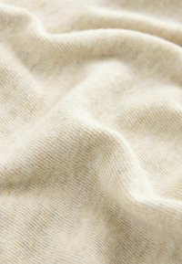Vaalea beige neulekangas, jossa on pehmeä rakenne, ja väri vaihtelee hienovaraisesti, samalla kun se näyttää sileältä ja hieman venytetyltä.