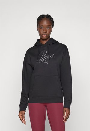 Sort hettegenser i bomull med lomme foran, med en metallisk Puma-logo og snorer. Kombinert med burgunder leggings.