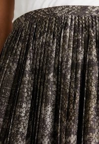 Detalle de una falda plisada con un estampado en serpiente en tonos gris y negro, combinada con una blusa blanca.