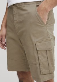 Kaki színű cargo rövidnadrág, pamut keverékből készült, oldalsó zsebekkel, laza szabású, és látható varrással az illesztéseknél.