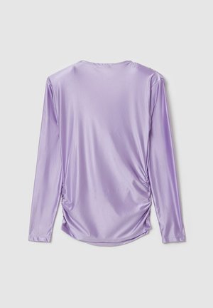 T-shirt à manches longues en lavande clair, fabriqué dans un tissu lisse et brillant. Présente des détails froncés sur les côtés et un col rond.
