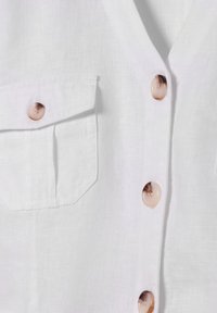 Weißes Leinenhemd mit einer Tasche, fünf großen beigen Knöpfen mit subtilen Mustern und einer weichen, strukturierten Oberfläche.