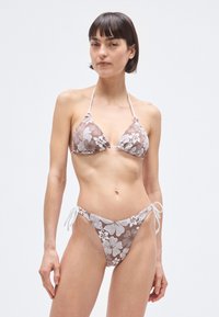 Brown floral bikini with white accents; triangle top with ties and side-tie bottoms. Smooth texture, featuring a white floral pattern on brown background.