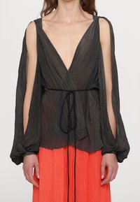 Haut plissé noir enroulé avec décolleté en V profond et manches longues. Présente une taille nouée et un design fluide, associé à une jupe orange vif.