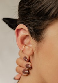 Goldene Creole mit kleinen funkelnden Akzenten, aus der Nähe vor einem verschwommenen Hintergrund zu sehen, getragen am Ohr einer Person.