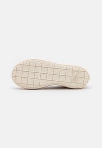 Semelle de chaussure beige avec motif en grille, formes d'étoiles en relief et logo "Puma" embossé près du talon sur fond blanc.