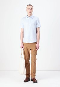 Lyseblå kortermet skjorte med knapper, beige chinos, brune sko og en hvit tote-bag. Glatt stoff, tilpasset passform, uformell stil.