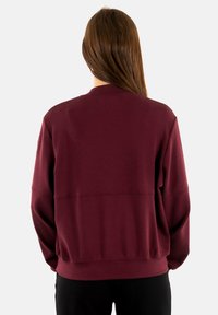 Felpa color bordeaux con scollo rotondo, vestibilità oversize, spalle scese e bordi a coste su polsini e orlo. Tessuto liscio e strutturato.