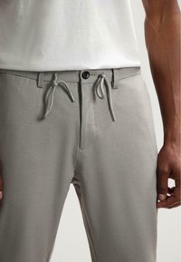 Lichtgrijze broek met een gestructureerd oppervlak, voorzien van een elastische tailleband met trekkoorden en een knoopsluiting aan de voorkant.