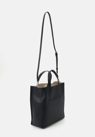 Bolso tote de cuero negro con una superficie texturizada, dos asas en la parte superior y una correa larga ajustable. Interior visible, que muestra un forro beige.