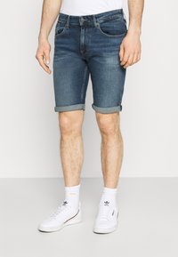 Shorts de denim en azul oscuro, con un corte clásico, dobladillos enrollados y diseño de cinco bolsillos, combinados con zapatillas blancas y calcetines.