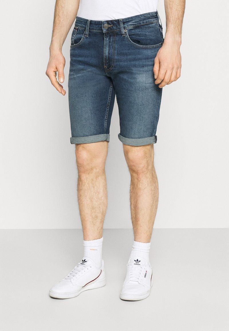 Shorts de denim en azul oscuro, con un corte clásico, dobladillos enrollados y diseño de cinco bolsillos, combinados con zapatillas blancas y calcetines.