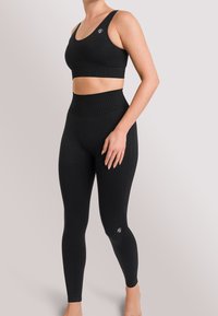 Black sports bra and high-waisted leggings made from textured fabric, featuring a ribbed waistband and logo accents on both pieces.