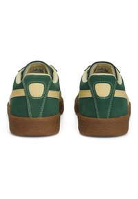 Sneaker in suede verde con accenti beige, retro arrotondato e suola in gomma testurizzata; presenta cuciture a contrasto e tallone rinforzato.