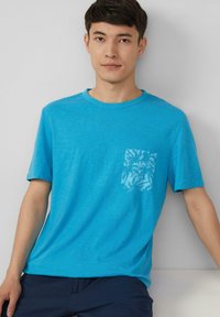 Turquoise katoenen t-shirt met korte mouwen en een ronde hals. Heeft een subtiel palmbomenbladpatroon op de linkerkant van de borstzak.