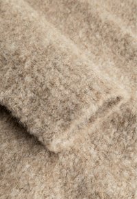 Beigen värinen neulottu kangas, jossa on pehmeä, pörröinen pinta ja taitettu hihansuun reuna.