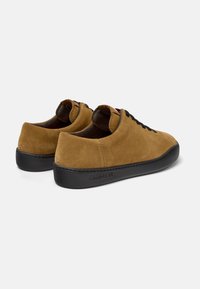 Zapatillas de ante marrón con suelas de goma negra, puntera redondeada y cordones negros. Presenta un sutil logotipo de la marca en el lateral y una textura suave.