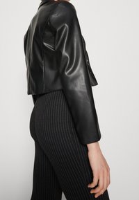 Musta nahkatakki, jossa on lyhyt malli, sileä pinta ja pitkät hihat, yhdistetty mustiin, kapea raidallisiin housuihin.