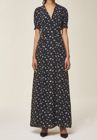 Svart maxiklänning med V-ringning, puffärmar och små blommönster i rosa och vitt. Mjukt tyg med en flödande design. Svarta skor.