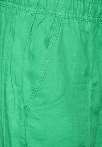 Green linen fabric showcasing a smooth texture with a gathered waistline and a detailed seam near a side pocket.