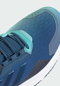 Miesten urheilukengissä on tummansininen verkkopinta, turkoosit yksityiskohdat, teksturoidut kuviot ja pehmustettu pohja, jossa on huomattava nauhoitusjärjestelmä.