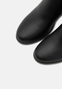 Black leather ankle boots with a smooth texture, rounded toe, and subtle stitching detail. The sole is flat and slightly raised at the heel.