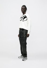 Sweatshirt branca com um logótipo gráfico preto, combinada com calças cargo de couro preto e ténis preto e branco com um design elegante.