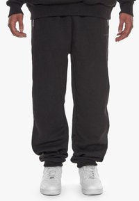 Black jogger pants made of soft fabric, featuring tapered cuffs and side zip pockets, worn with white sneakers.