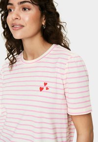 T-shirt en coton avec des rayures roses et blanches, col rond, manches courtes, présentant trois motifs de cœurs rouges sur le côté gauche de la poitrine.