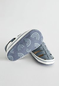 Blå canvas-sandaler med öppen design, vit sula och mönstrade gummibottnar med ljusblå regnbågar och böjda linjer.