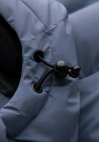 Niebieska pikowana kurtka z czarną podszewką, z zapięciem na ściągacz i okrągłym czarnym zatrzaskiem. Gładka tekstura z starannymi detalami szwów.