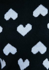 Svart stickad tyg med ett mönster av vita hjärtan. Hjärtana är solida och jämnt fördelade, vilket ger en texturerad utseende.