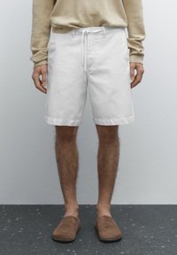 Hvide bomuldsshorts med en snor i taljen, med lige snit og opsmøgte kanter, parret med brune slip-on sko.
